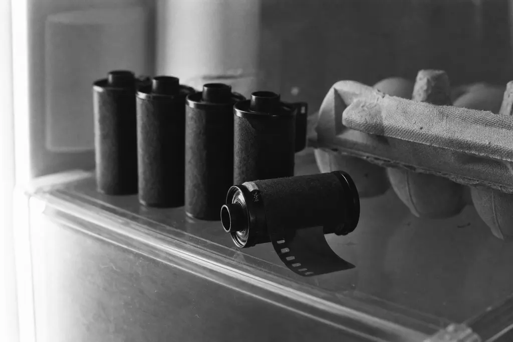 Kleinbildpatronen stehen aufgereiht im Kühlschrank, aus einer ragt ein Stück Film heraus (mit AI erstelltes Bild)