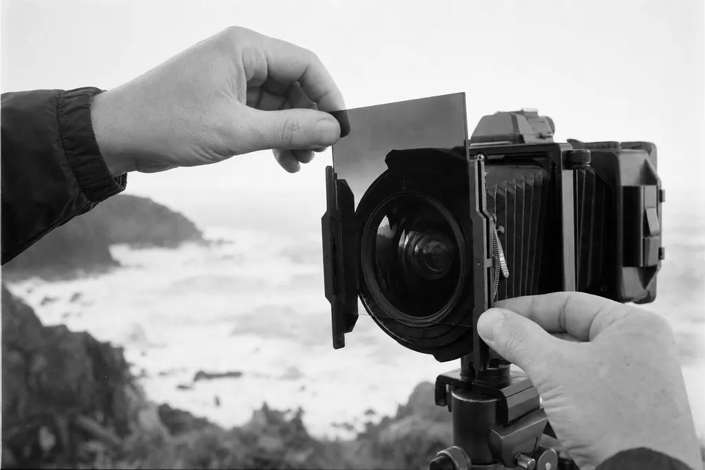 Quadratischer Graufilter wird an der Küste in einen Filterhalter vor dem Objektiv geschoben (mit AI erstelltes Bild)